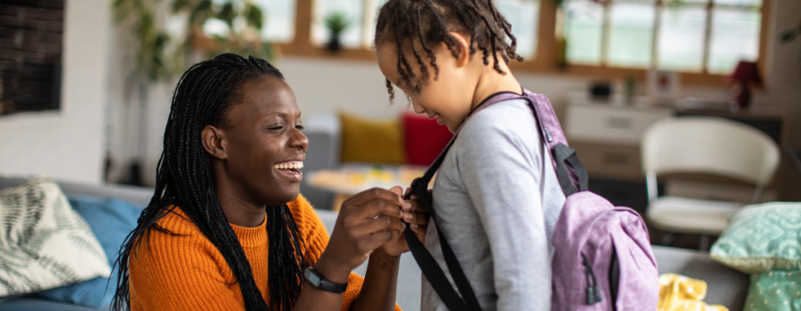 A Black parent putting on a backpack onto their young child