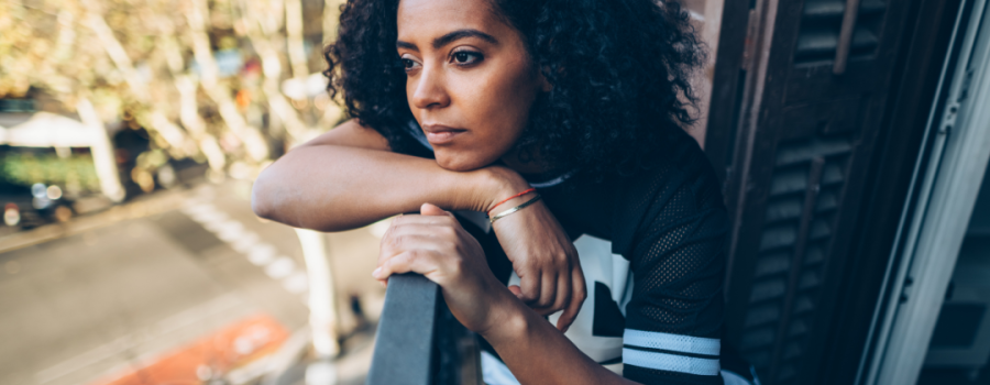 A Black woman looking over a balcony looking sad