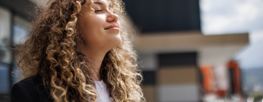 A young woman with curly hair looking upward and breathing in deep