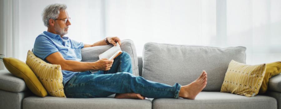 Older man sitting on a couch reading a book