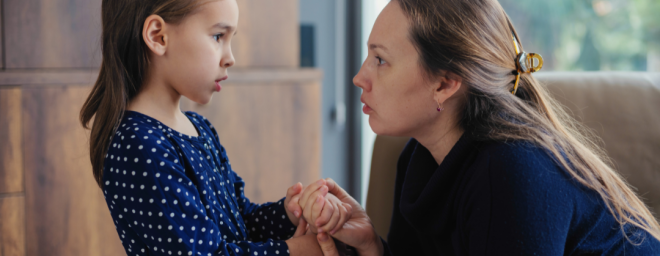 A female adult holding her worried child's hand