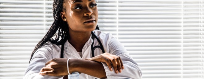 A young black woman sitting near an office window looking pensive