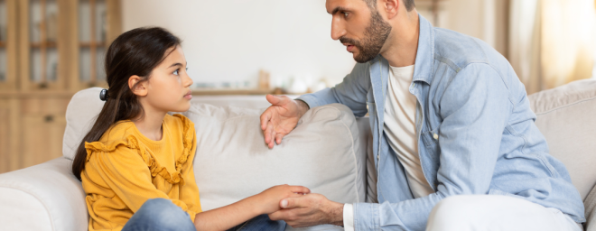 An adult male/dad talking to you younger female child while holding her hand