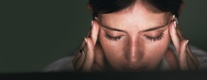 A close up photo of a woman holding her head at her temples