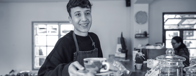 A teenage boy barista handing a cup of coffee to a customer