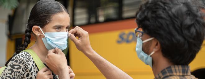 Photo of an adult putting a face mask on a little girl in a school gym