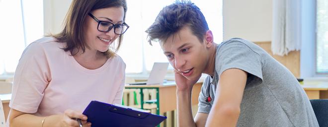 A woman with glasses helping a teenage boy